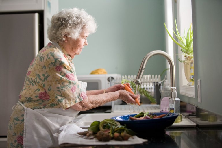Oudere dame wast groente in de keuken