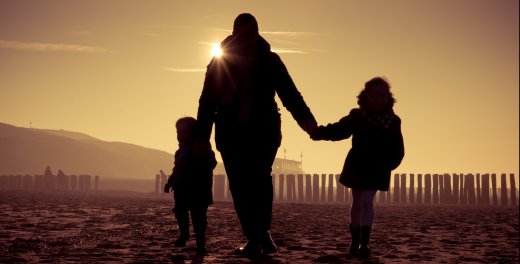 Ouder met twee kleine kinderen op het strand met avondzon. 